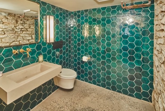 A bathroom wall tiled in deep teal hexagon tile beside a stone-faced wall