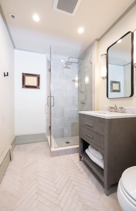 A herringbone tile floor running up to a glass shower enclosure