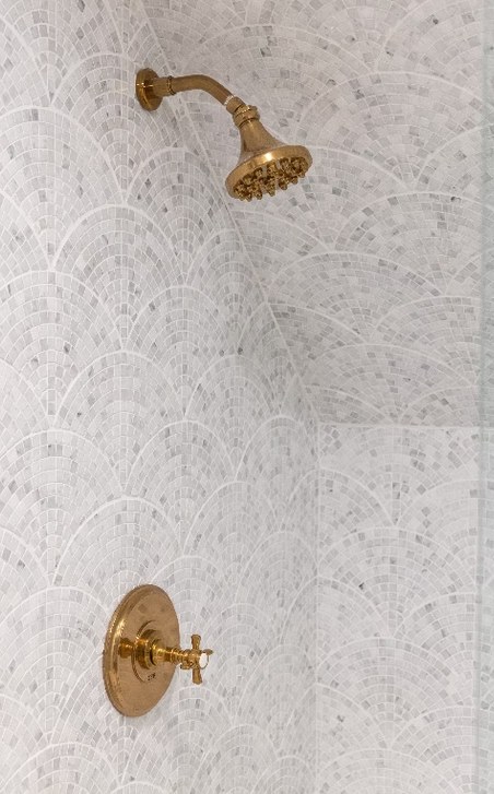 A carrara marble shower wall with a brass shower head and control